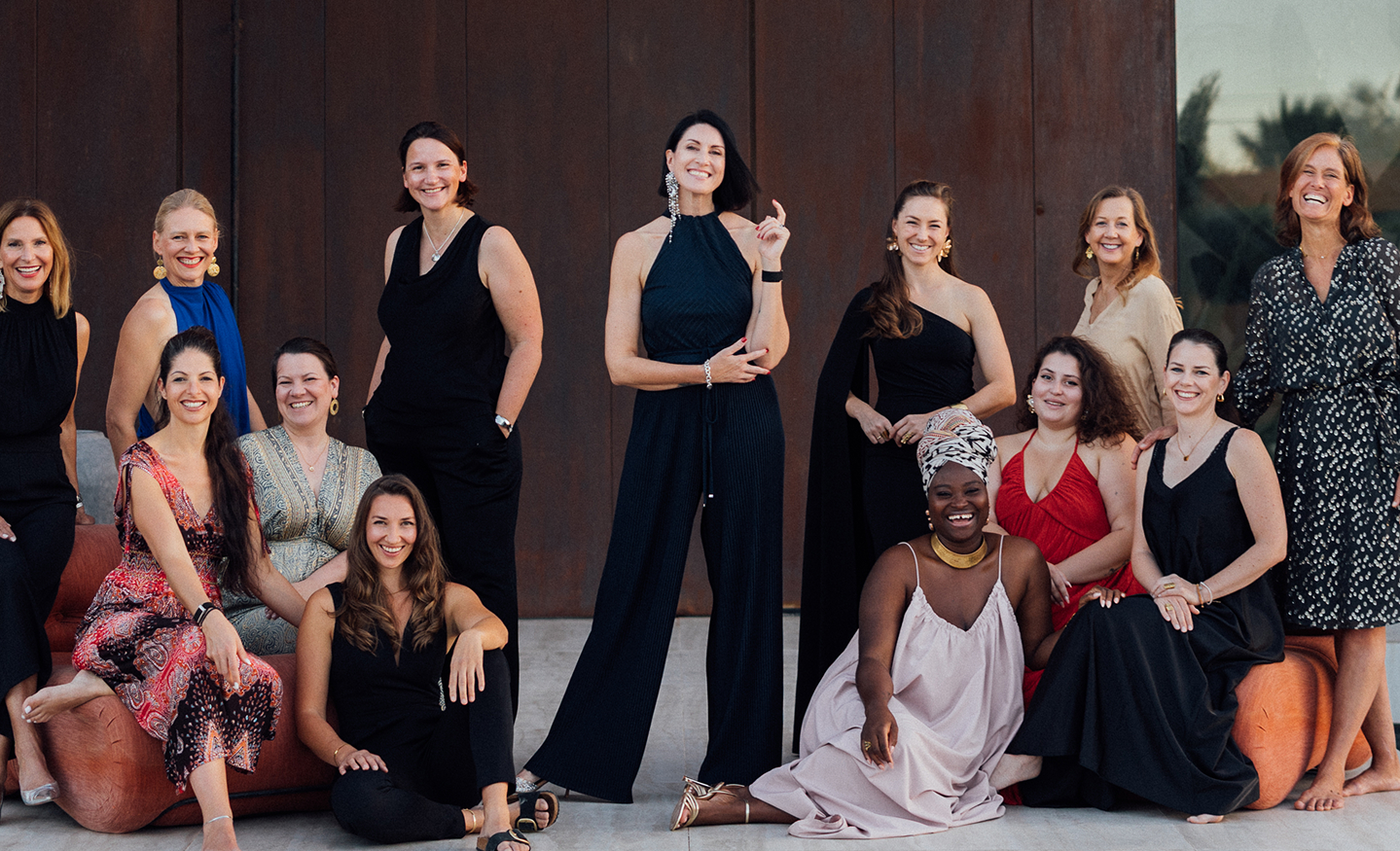 Gruppe von elf lächelnden Frauen in eleganter Kleidung vor einer dunklen Wand