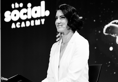 Frau in weißem Blazer vor dem Logo „the social academy“ auf einer Bühne