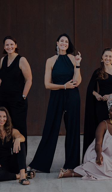 Mehrere Frauen in eleganten schwarzen Outfits posieren vor einer dunklen Wand