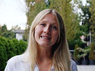 Porträt einer lächelnden blonden Frau im Freien vor Bäumen und einem Haus