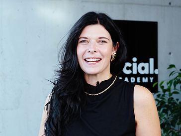 Porträt einer lächelnden Frau vor einem „Social Academy“-Schild